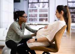 A doula consults with a pregnant woman, placing a hand on her stomach.
