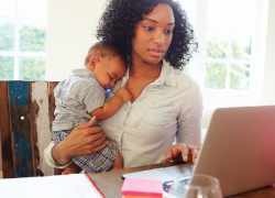 A woman holds an infant while using a laptop
