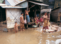 A Bangladeshi family stands outside their home, which is surrounded by floodwaters.