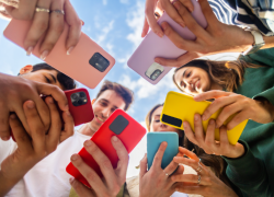 Shot from below, six young people stare at the screens of their brightly colored phones.