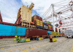 Several workers unload cargo from large containers at a port.