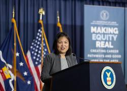 Acting Secretary Julie Su giving a speech at a podium with a sign that says "Making Equality Real" in the background.