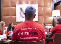 Several workers sit and talk with Acting Secretary Su at The Venetian Resort. One worker’s red shirt, seen from the back, has the words “Culinary Union #226. Unite Here! Bartenders Union #165.” 