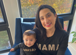 A woman with dark hair sits by a window, holding a baby in her lap.