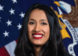 Image of a brown woman with long black hair who is smiling in front of the American and DOL flags.