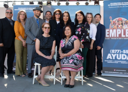 Eleven people in business attire pose in front of an EMPLEO program banner with the hotline.