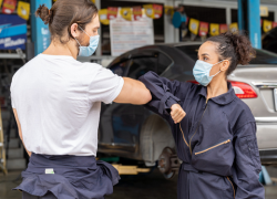research question for gender wage gap A male and female mechanic wearing masks bump elbows