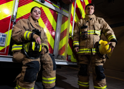 Wearing firefighting gear, Airman 1st Class Nicolette Chilson and Airman 1st Class William Phelp stand in front of a firetruck at Nellis Air Force Base, Nevada. U.S. Air Force Photo by Airman 1st Class Trevor Bell. 