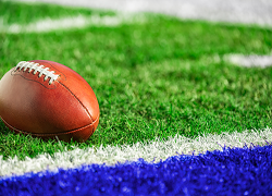 A football rests on a football field. The grass is striped with white and blue paint.