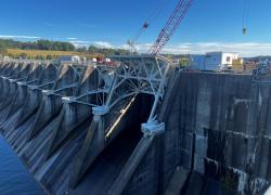 A view of a large dam with construction equipment on top, including a crane.