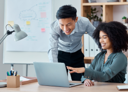 Two co-workers look at a computer in an office environment.