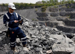 An MSHA inspector uses a tablet while standing on a pile of rocks at an outdoor mining site.