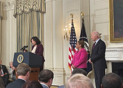 Acting Secretary of Labor Julie Su stands at a podium at the White House with President Joe Biden.