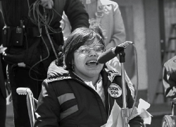 Black and white photo of Judy Heumann speaking into a microphone at a rally.
