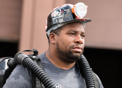 A male mine rescue worker wearing a hardhat and oxygen tank