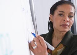 An older Black woman in professional dress looks at the camera while holding a marker. 