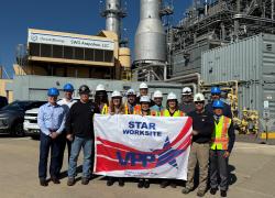 A group of people in hardhats stand in front of an energy plant holding a banner that says "STAR Worksite, VPP"