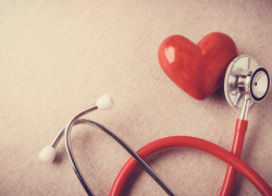 A red stethoscope laying next to a red heart.