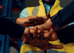 A pair of hands overlapping with each other with an individual in the background with a yellow vest. 