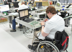 A worker who uses a wheelchair works in a high tech environment constructing solar panel components