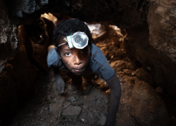 A boy wearing a headlamp works underground in a mica mine.