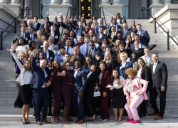 Julie Su and dozens of people in suits and professional attire pose for a photo on the steps of the White House. They are smiling and striking playful poses. 