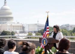 Women's Bureau Director Wendy Chun-Hoon speaks at a podium with the Labor Department seal outdoors. The U.S. Capitol is visible in the background.