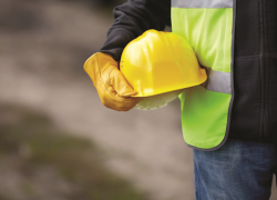 A worker wearing safety gear holds a hard hat.