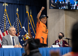 A woman wearing an orange shirt stands and gestures enthusiastically during a panel discussion at the Workers’ Voice Summit.