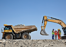 A group of construction workers stand by some large machinery on a worksite.