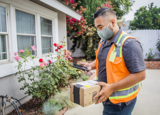 A male worker wearing a safety vest delivers a package to a home
