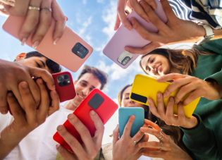Shot from below, six young people stare at the screens of their brightly colored phones.