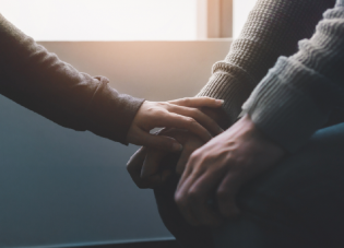 Close-up of a therapist reaching out toward the hands of a patient in a comforting gesture