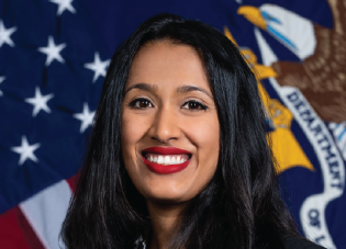 Image of a brown woman with long black hair who is smiling in front of the American and DOL flags.