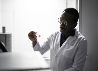 A black scientist in a white lab coat examines a test tube.