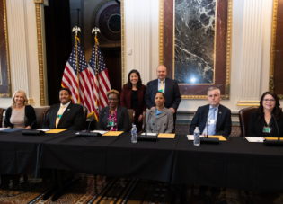 John Ladd stands next to Acting Secretary Su behind six panelists at the 2024 Cybersecurity Apprenticeship Event.