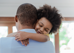 A young girl hugs her father around the neck.