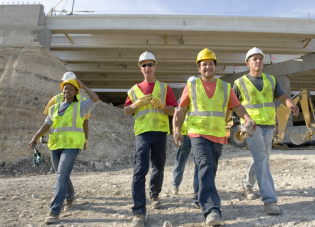 Construction workers in safety gear walk away from a construction site.