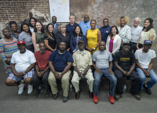 About two dozen people pose for a group photo in front of a brick wall.