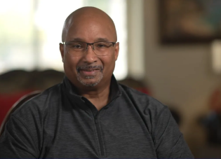 Derek Smith, wearing glasses and a dark, zip-up shirt with a half collar.