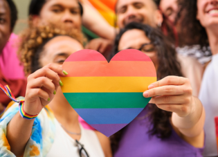 A group of diverse people standing together with two in front holding a rainbow heart.