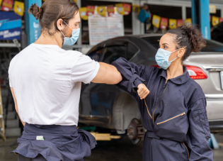 A male and female mechanic wearing masks bump elbows