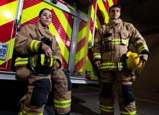 Wearing firefighting gear, Airman 1st Class Nicolette Chilson and Airman 1st Class William Phelp stand in front of a firetruck at Nellis Air Force Base, Nevada. U.S. Air Force Photo by Airman 1st Class Trevor Bell. 