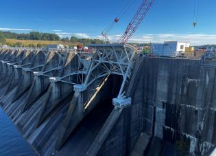 A view of a large dam with construction equipment on top, including a crane.