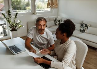 Two people sit at a table with a laptop and financial documents