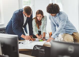 Três funcionários corporativos sentam-se a uma mesa, examinando um arquivo. 