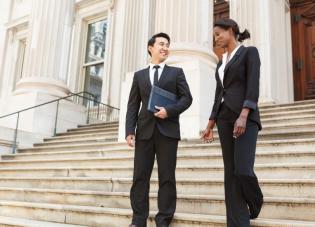 A man and a woman in professional dress walk down the steps of a government building.