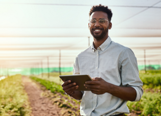 A man standing in a crop field uses a tablet.