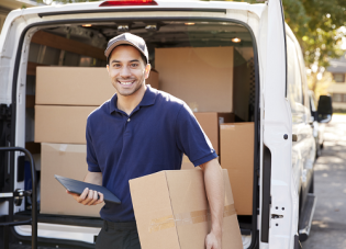 A delivery worker carries a large cardboard box to the front porch of a home, and knocks on the door.