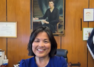 Acting Secretary of Labor Julie Su sits at her desk. A painting of former Secretary of Labor Frances Perkins is on the wall behind her.